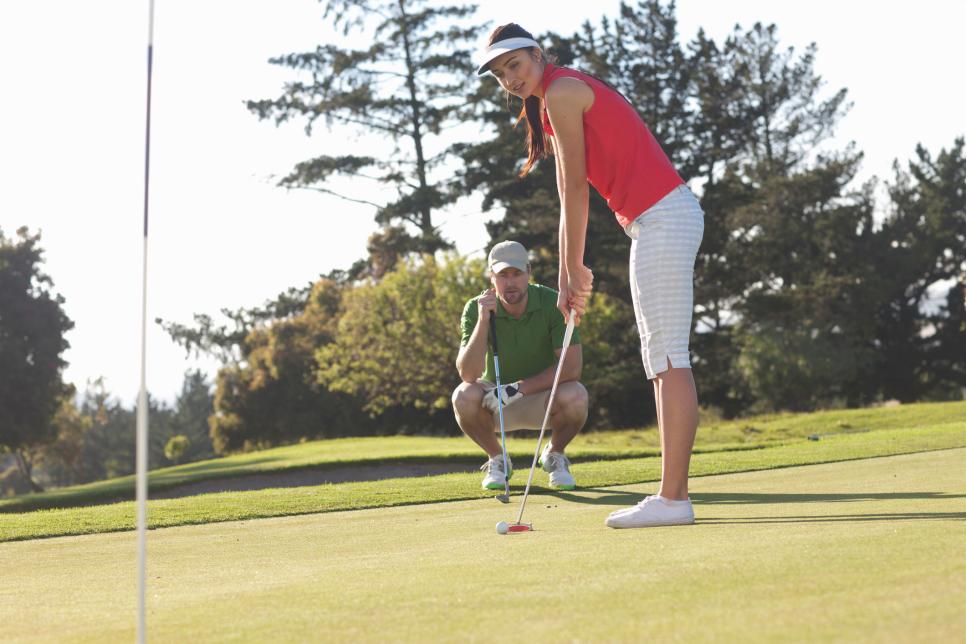 Young female golfer on golf course with trainer