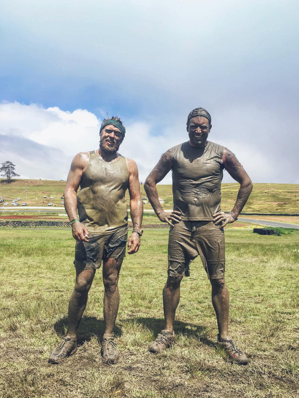 Two happy men standing together after completing a mud run challenge