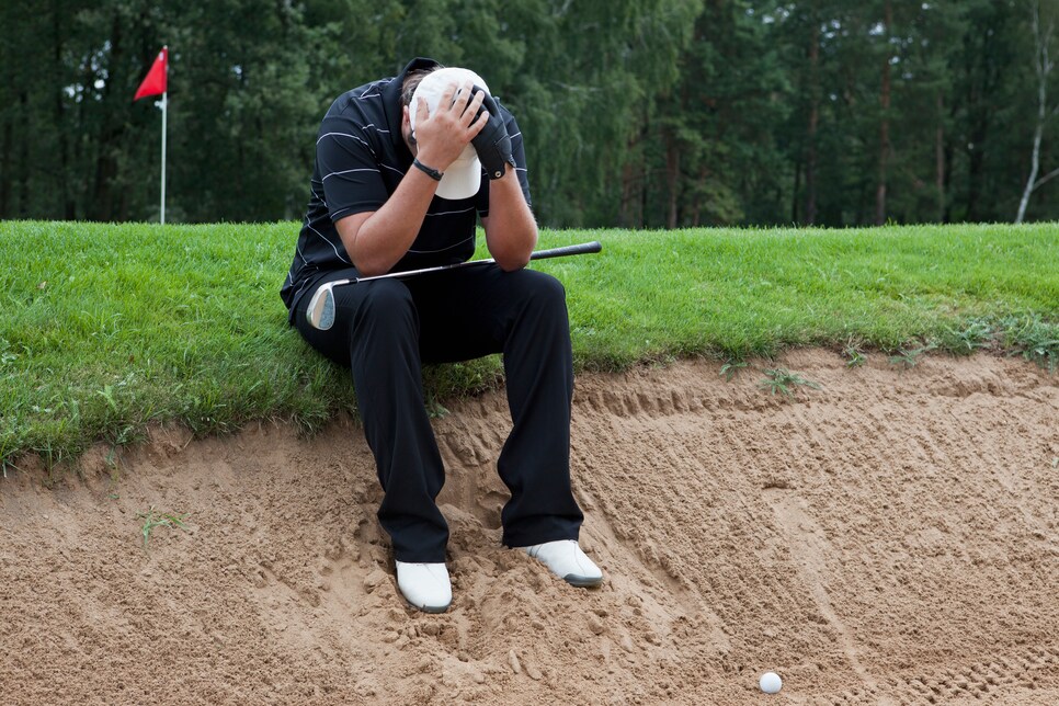 A golfer sitting at the edge of sand trap, head in hands