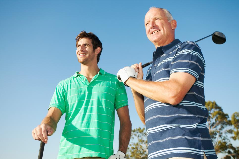 Young man and senior man holding golf clubs outdoors