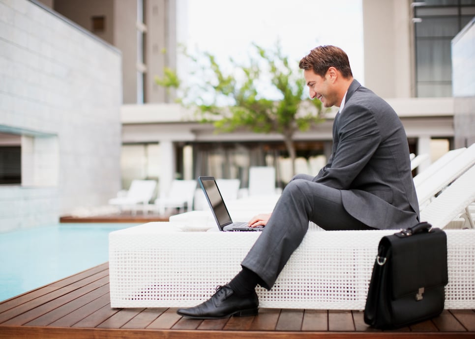 Businessman using laptop on lounge chair near swimming pool