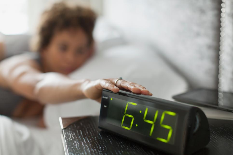 Woman reaching for snooze button on alarm clock.