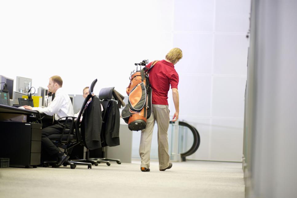 Businessman carrying golf clubs in office