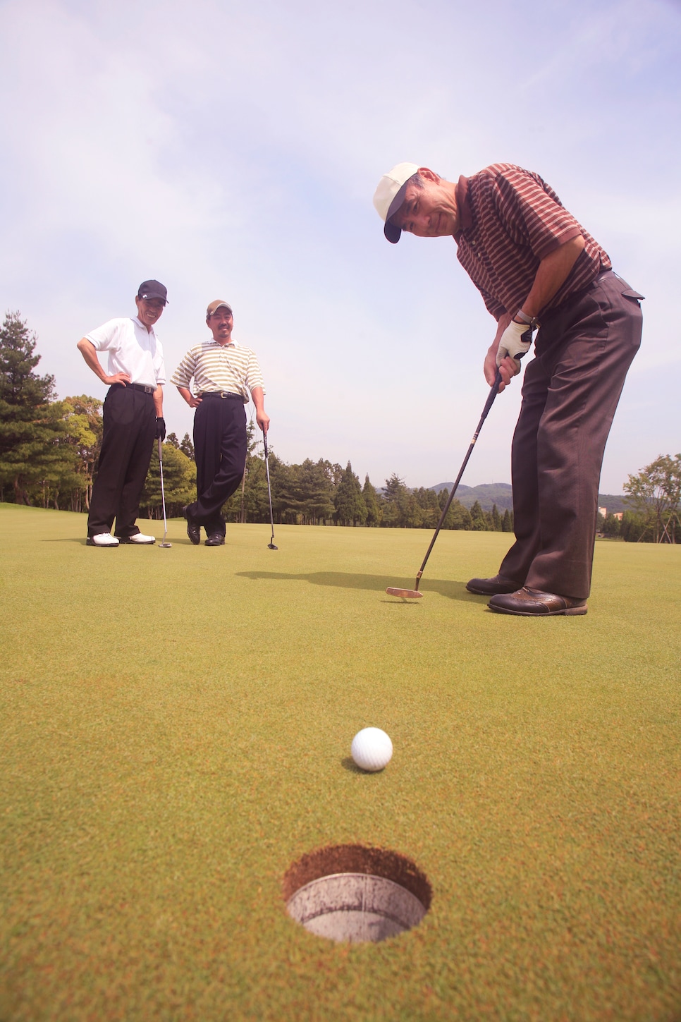 Three mature men playing golf (focus on hole in foreground)