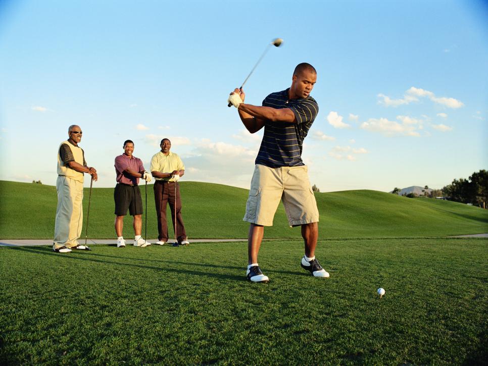 Male golfer driving ball, friends watching (blurred motion)