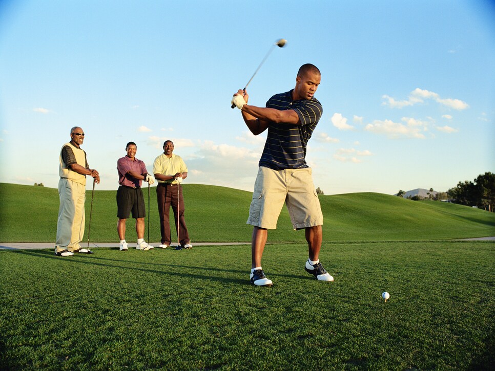 Male golfer driving ball, friends watching (blurred motion)