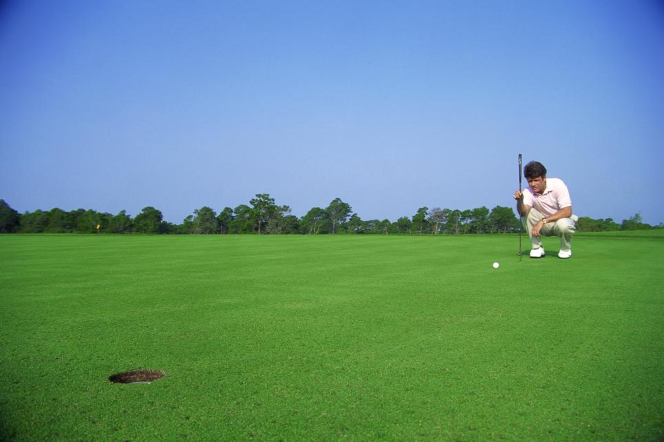 Man squatting to line up his putt on a golf course