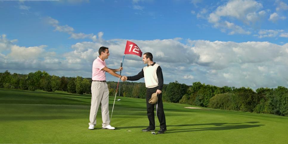 Two male golfers, standing on green shaking hands