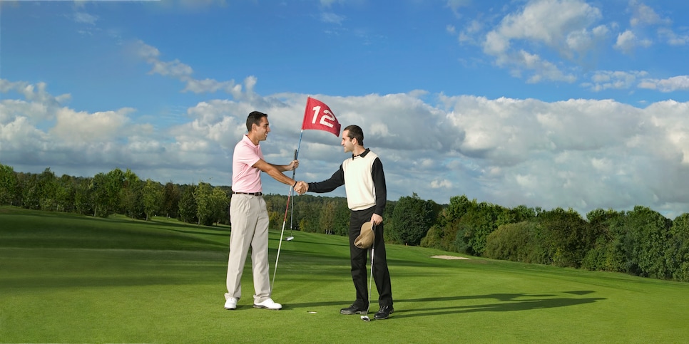 Two male golfers, standing on green shaking hands