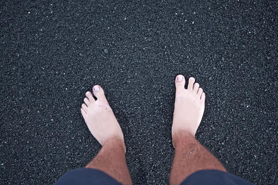Barefeet with sandal tan on black sand beach