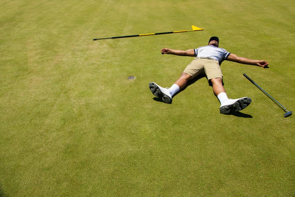 Distraught golfer lying on putting green.