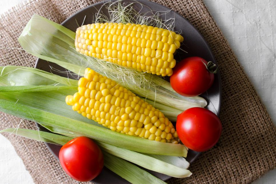 Boiled corn and raw tomatoes in a plate. Tasty and healthy vegetarian meal