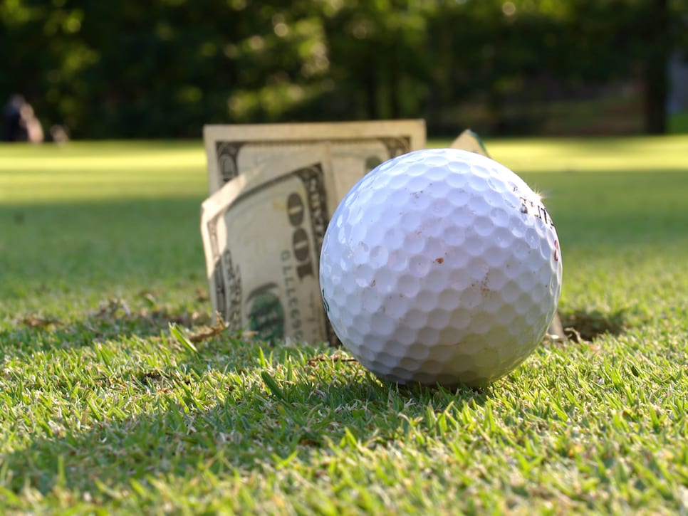 Closeup of golf ball by hole with $100 bills sticking out.