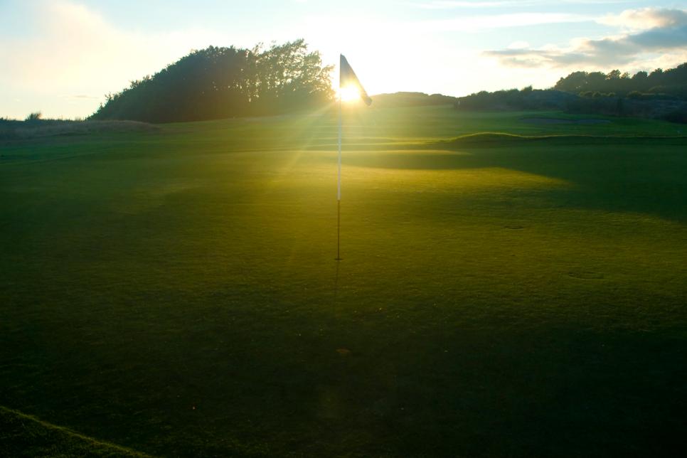 Sun setting through flag on golf course