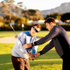 A young golf coach corrects the swing of a golfer during a lesson at a golf course.