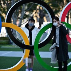 Mask-clad people pose with an installation of the Olympic rings in Tokyo on February 28, 2020. - The International Olympic Committee is "committed" to holding the 2020 Games in Tokyo as planned despite the widening new coronavirus outbreak, the body\'s president has pledged. (Photo by CHARLY TRIBALLEAU / AFP) (Photo by CHARLY TRIBALLEAU/AFP via Getty Images)