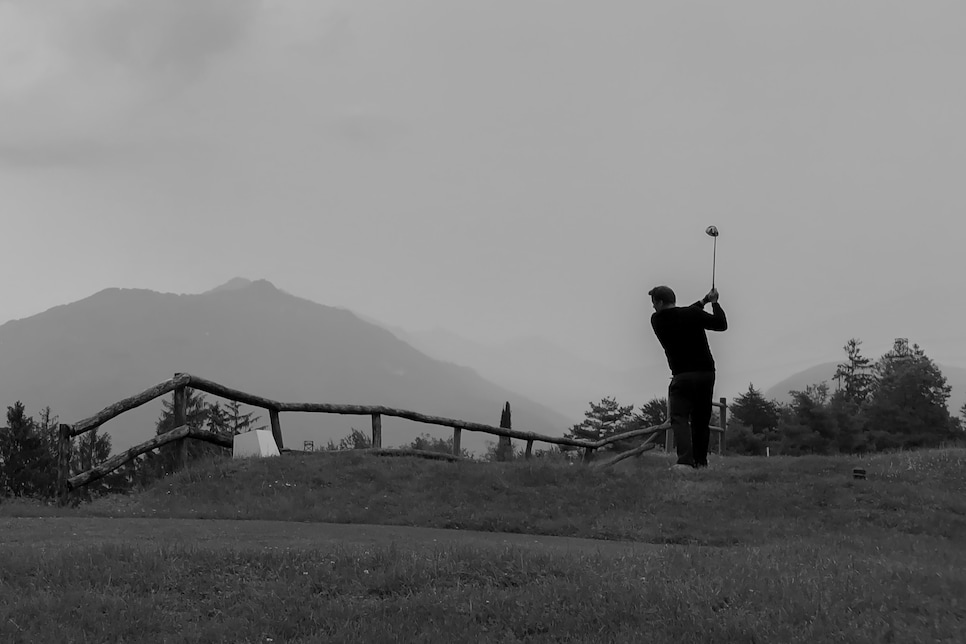 Golfer Teeing Off on Golf Course with Mountain and Overcast Sky in Italy.