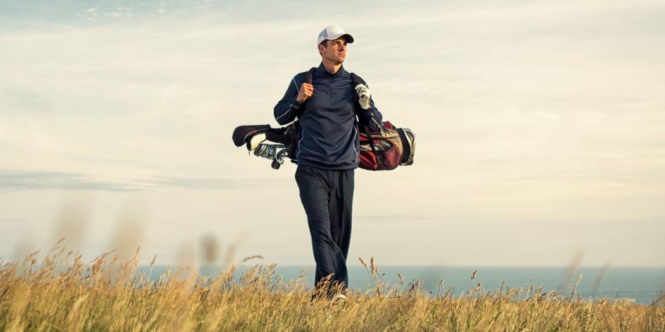 A male adult golfer walks to the green atop a links golf course in England.