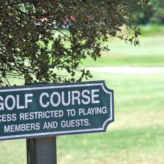 A small sign telling pedestrians that access to a golf course is "restricted to playing members and guests".
