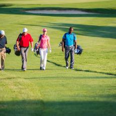 Four golfers talking while walking on the golf course.