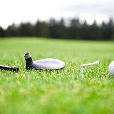 broken golf driver and tee with the golf ball next to them  on a golf course